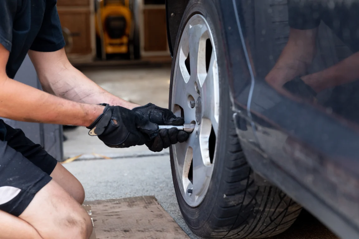 A mobile tyre technician wearing gloves tightens the wheel of a car using a socket wrench.